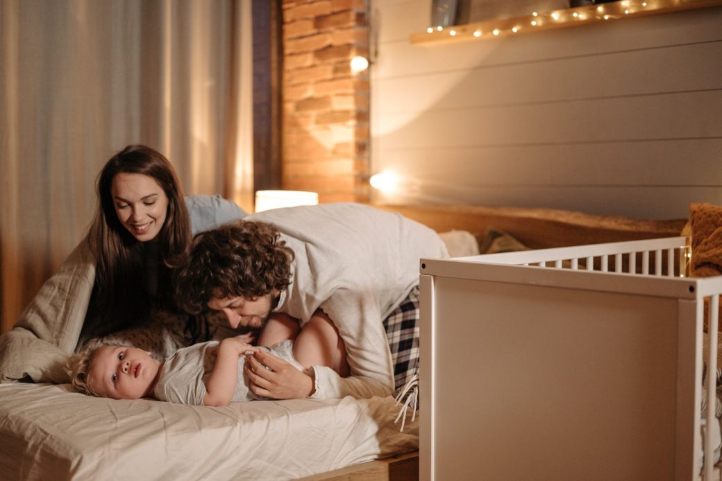 A joyful family moment with parents and child in a cozy, warmly lit bedroom.