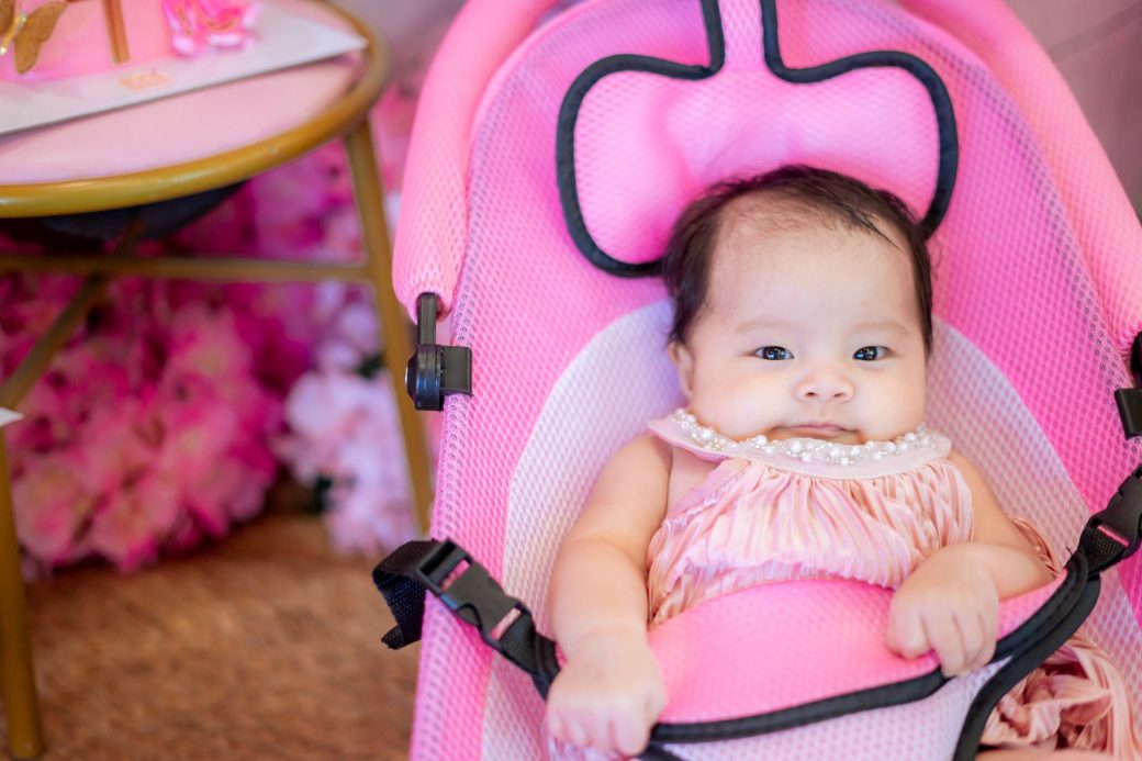 Charming baby girl in a pink bouncer chair adds cuteness to an indoor setting.