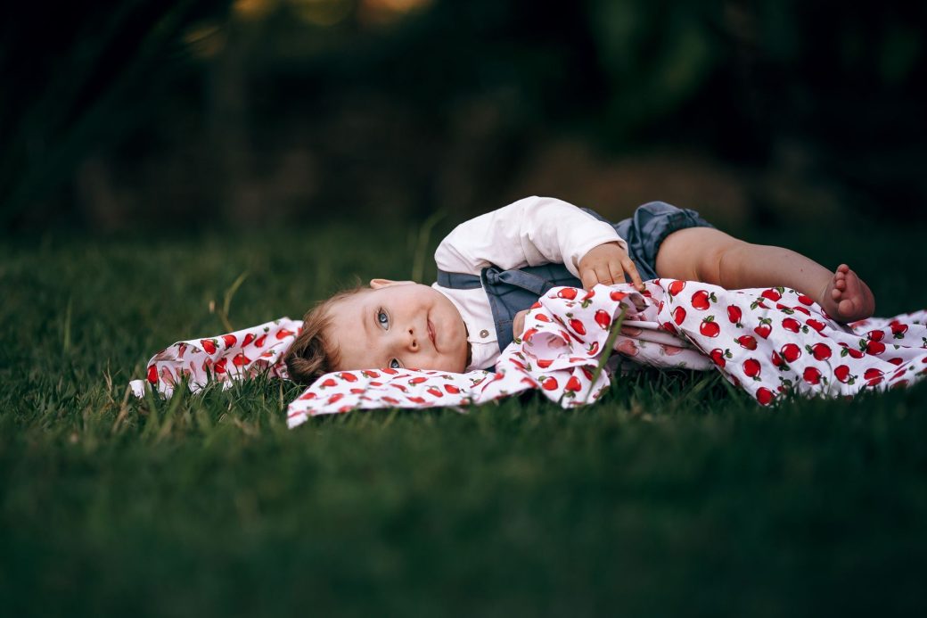 Adorable baby lying outdoors on a patterned blanket in the sun.