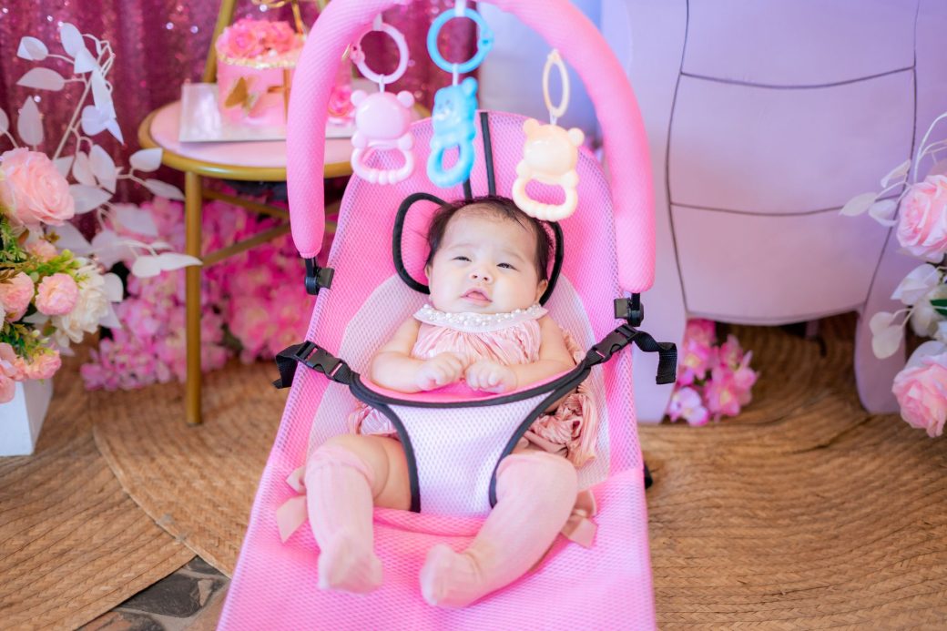 Charming baby girl in a pink bouncer surrounded by flowers, perfect for family and lifestyle themes.