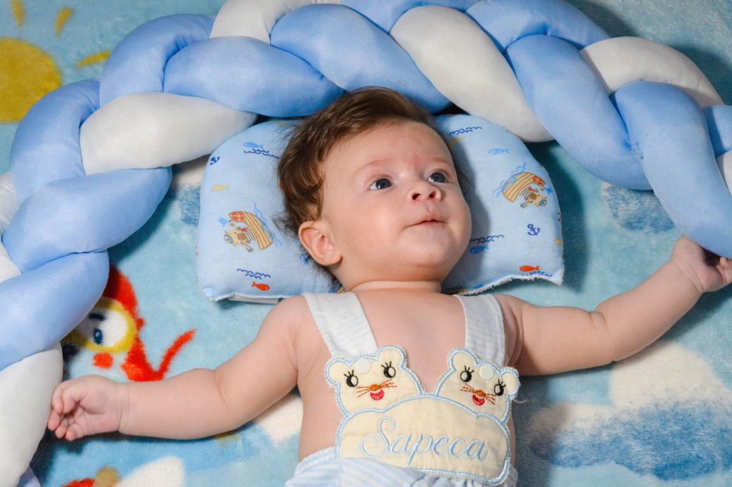 Cute baby in onesie resting on a cozy blue-themed bedding with playful designs.