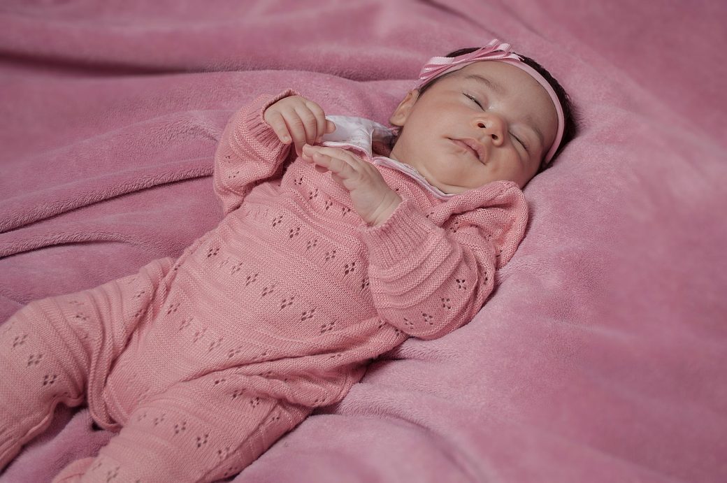 A serene baby girl peacefully sleeping on a cozy pink blanket, dressed in pink knitwear.