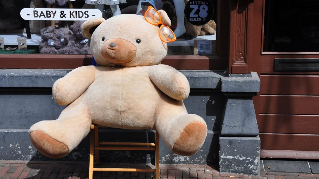 A giant teddy bear with orange glasses sits outside a toy store window display.