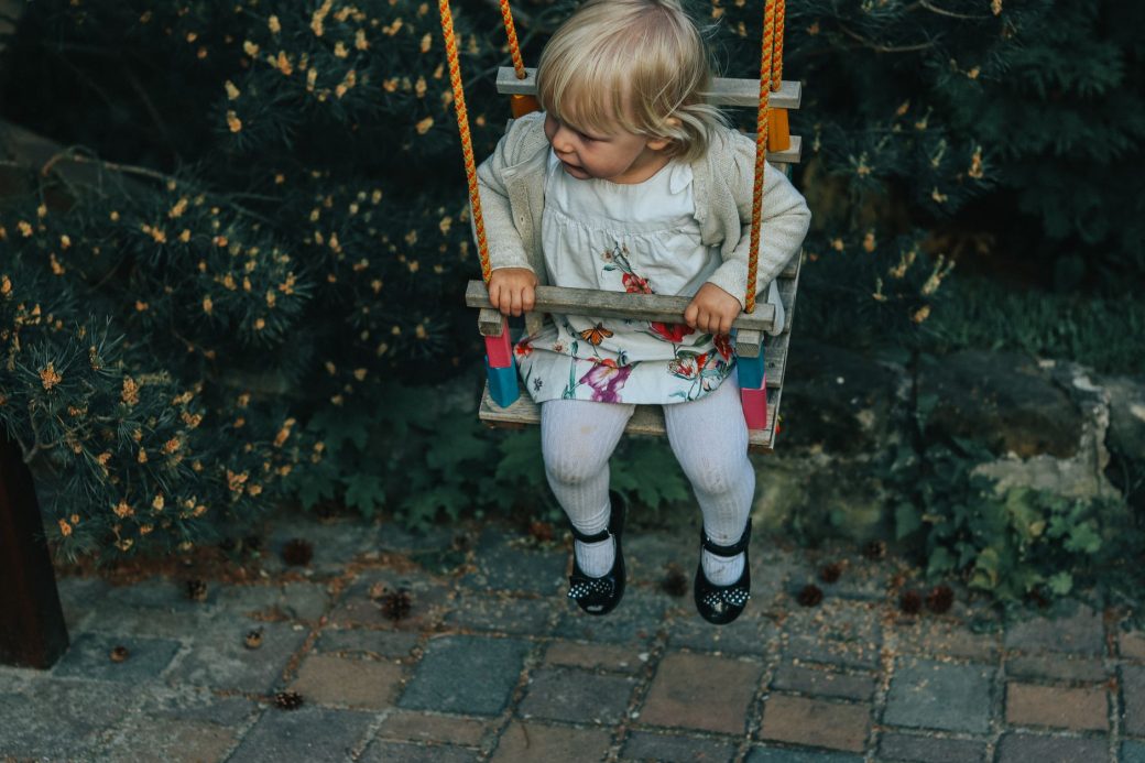 A cute toddler on an outdoor swing surrounded by lush greenery in a Prague park.
