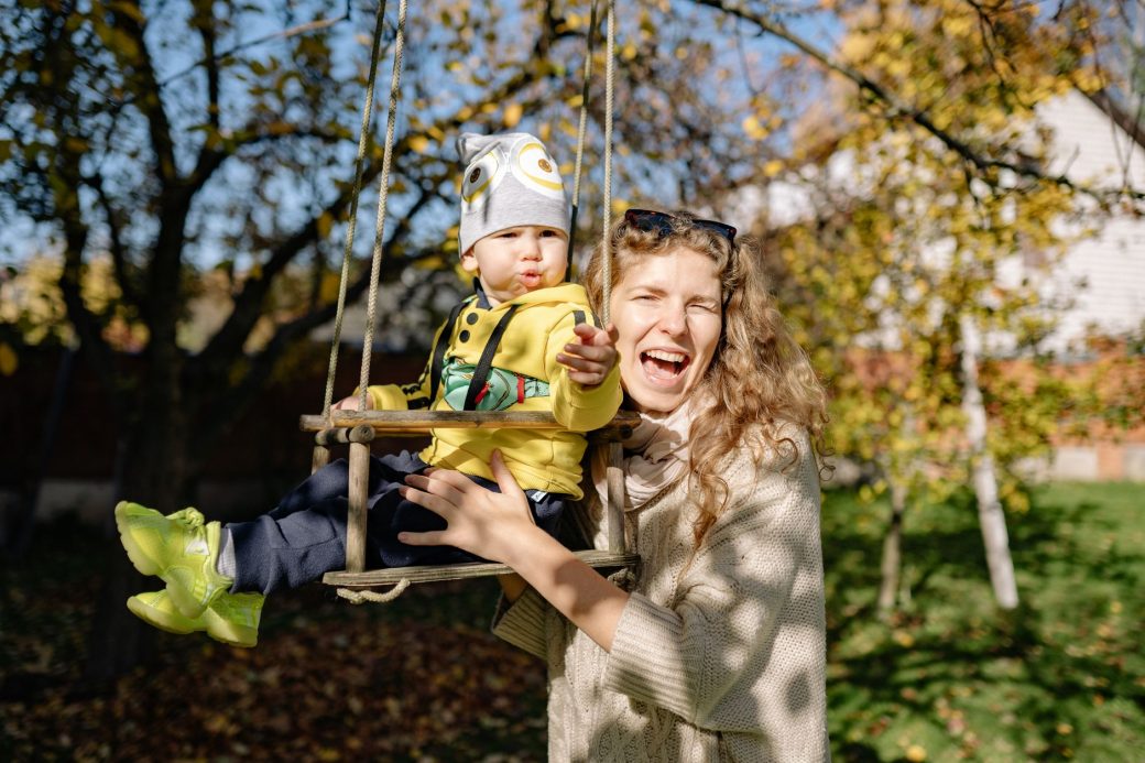 A happy mother swings her cheerful toddler in a bright outdoor setting.