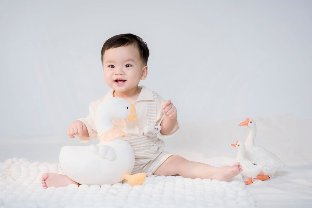 Cute toddler sitting and smiling with toy ducks, creating a playful childhood moment.