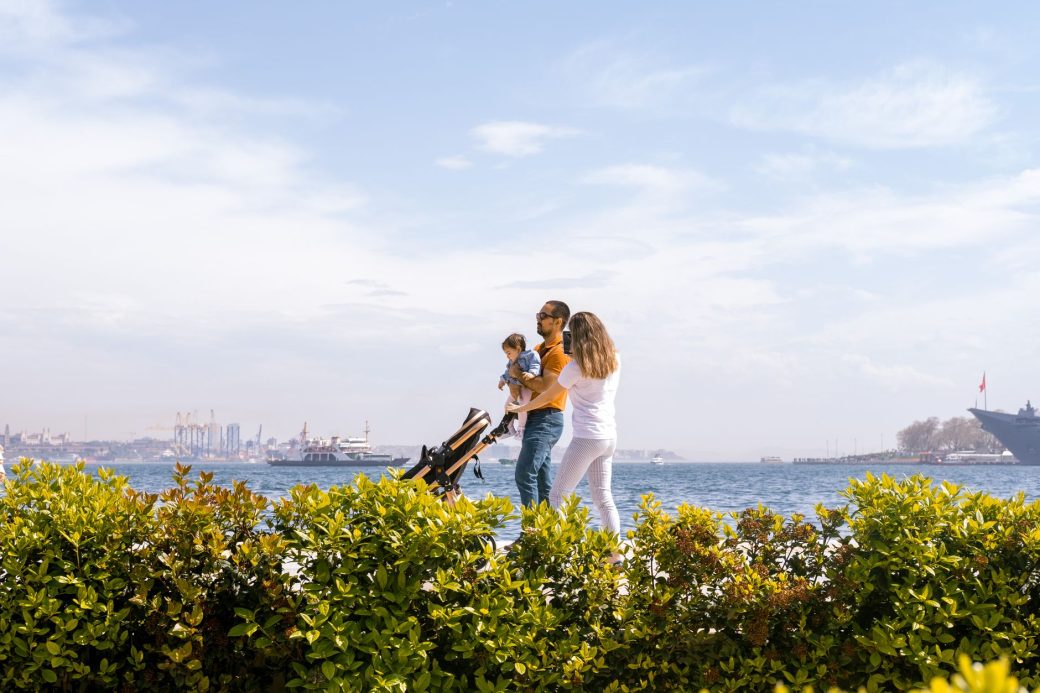 A family enjoys a walk along the seaside promenade under a clear, sunny sky.