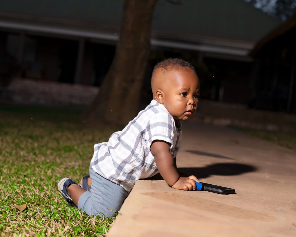 Adorable baby crawling on pathway with toy during a sunny day outdoors.