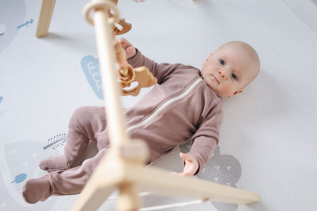 Cute baby in a cozy onesie playing with wooden toys on a soft mat indoors.