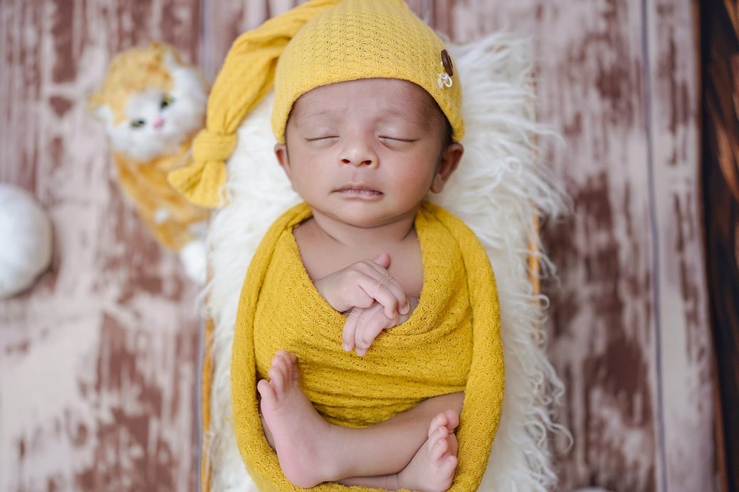 Adorable newborn baby peacefully sleeping in a yellow knitted wrap with a matching hat on a soft blanket.