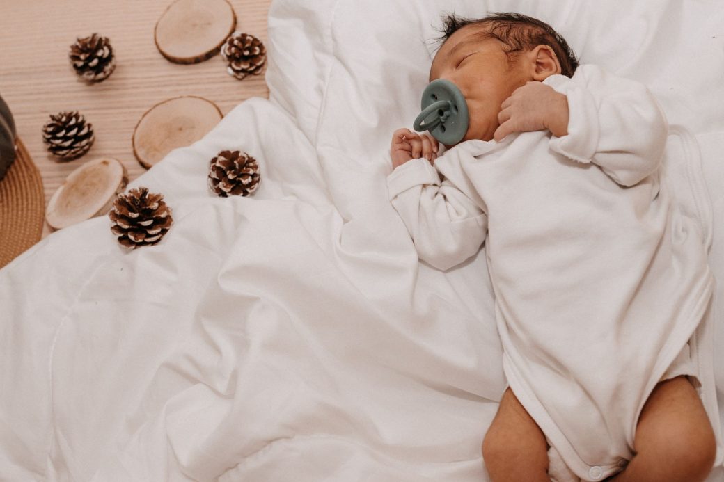 A serene baby sleeps with a pacifier amidst festive Christmas decor and pine cones.