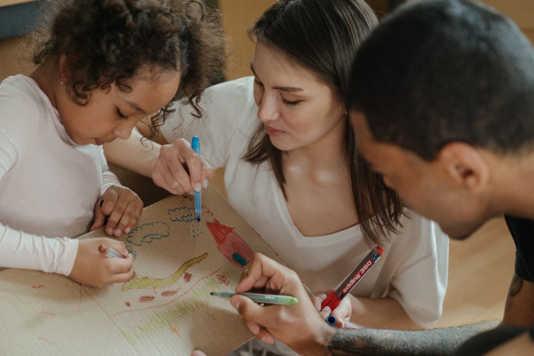 A family drawing together on cardboard, expressing creativity and spending quality time.