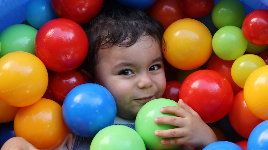 Adorable child smiling and playing in a vibrant ball pit indoors.