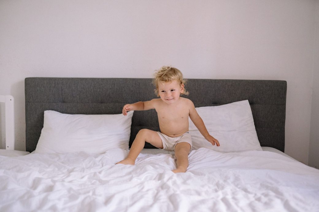 A happy toddler sitting on a large bed with white linens, expressing innocence and joy.